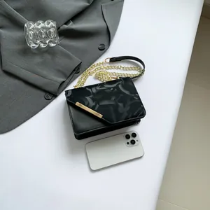 Chic black crossbody bag with textured pattern and gold metal bar on white background