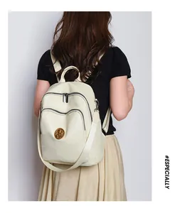 Detail of cream leather backpack featuring vintage gold crest and multi-zipper pockets