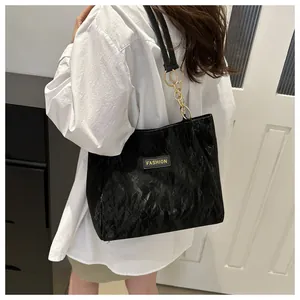 Detail van zwarte geplooide shopper met gouden kettingriem en Fashion-label aan de zijkant
