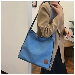 Detailed view of the blue canvas tote bag with brown leather logo patch and metal buckle
