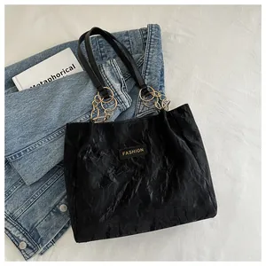 Detail van zwarte geplooide shopper met gouden FASHION-label en metalen ringketting