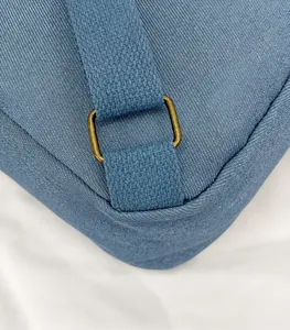 Macro detail of blue canvas backpack showing bronze metal ring and strap connection