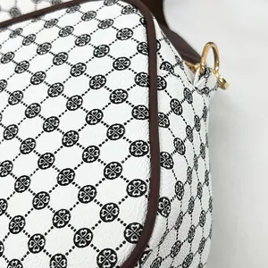 Close-up of cream shoulder bag with black clover pattern and gold metal ring detail