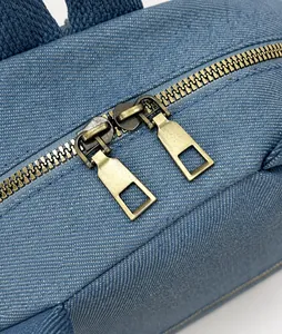 Detailed close-up of smooth gold metal zippers on premium blue denim fabric backpack