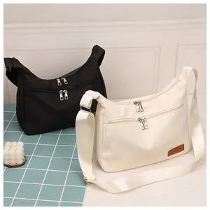 Detail of minimalist Oxford cloth crossbody bags in black and beige with front zipper pockets