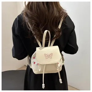 Dettaglio mini zaino in pelle PU crema con ricamo a farfalla rosa e stampa di ciliegie