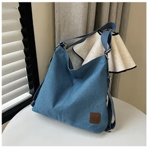 Detail of blue denim shoulder bag with leather patch and silver metal buckle adjustment