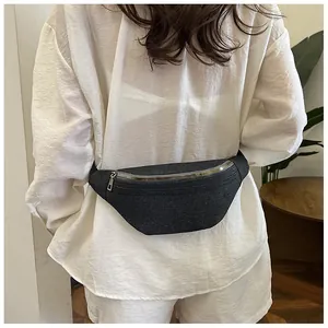 Close-up of a crescent denim waist bag in dark gray worn with a casual white outfit