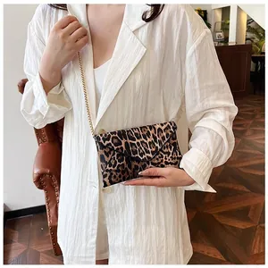 Detail of leopard print envelope clutch featuring golden chain strap on model