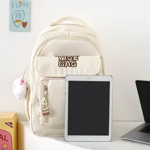 Close-up of beige school backpack with YIGE BAG logo and cute plush charms