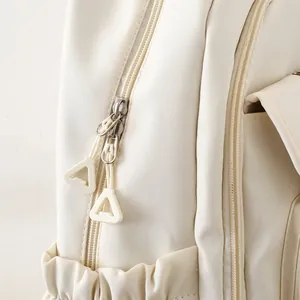 Detail view of durable metal zippers and elastic side pocket on cream backpack