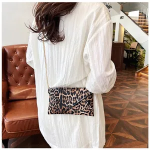 Leopard print envelope clutch bag with gold chain strap shown on a model in a cafe setting