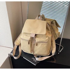 Detalle de mochila de lona beige con cordón ajustable, solapa y bolsillos con cremallera