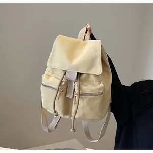Detalle de mochila de lona beige con cierre de cordón y bolsillos con cremallera dorada