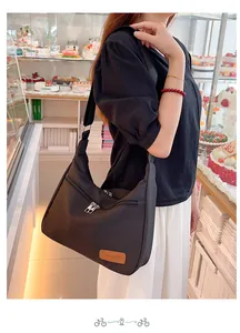 Detail of black crescent oxford cloth crossbody bag with front zipper pocket on model