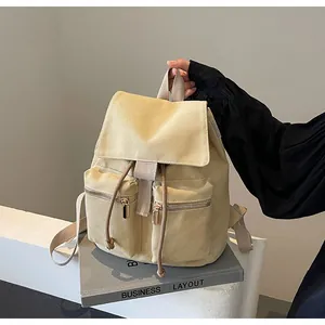 Detalle de mochila de lona caqui con cordón y bolsillos delanteros con cremallera
