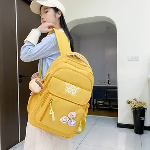Detail of a bright yellow high-capacity backpack with cute badges and plush keychain pendant