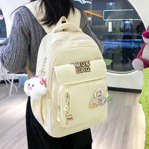 Detail view of cream school backpack featuring cute badges and plush charms on nylon material