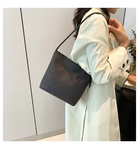 Dettaglio della borsa a tracolla grigia a pois indossata da una modella con trench minimalista