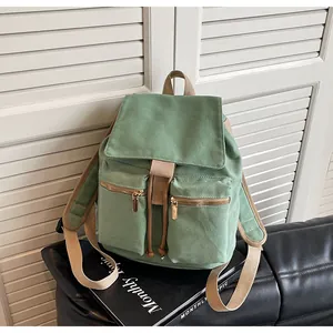 Detalle de mochila de lona verde claro con cierre de cordón y dos bolsillos frontales