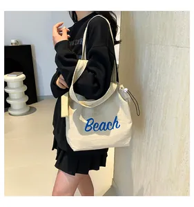 Detalle del bolso tote de lona crema con letras Beach en azul y ajuste de cordón lateral