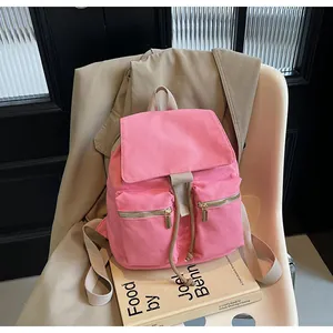 Detalle de mochila de lona rosa con correas crema colocada sobre libros y una silla