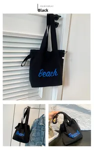 Detalle de bolsa tote de lona negra con letras Beach azules y cordón de ajuste lateral