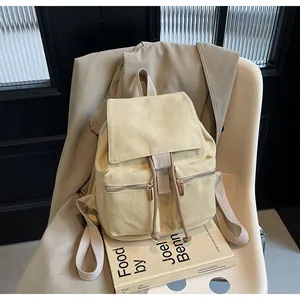 Detalle de una mochila de lona beige con bolsillos delanteros sobre una silla blanca