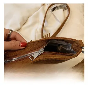 Detailed close-up of the silver metal zipper and brown suede texture on a crossbody bag