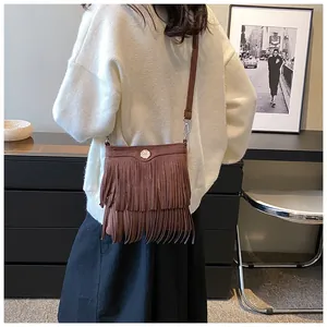 Brown tassel crossbody bag in frosted suede finish shown on model with metal buckle detail