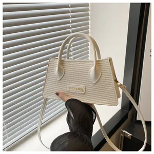 Detail of cream woven leather handbag with dual round handles and brand plate held by hand