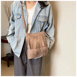 Detail of a brown suede crossbody bag featuring three-layered fringe and metal buckle
