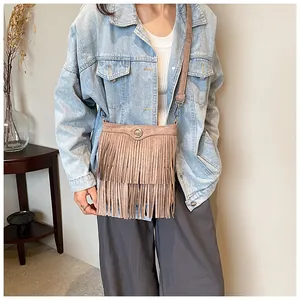 Detail of light brown faux suede crossbody bag featuring long fringe and a round buckle