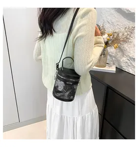 Detail of black cylindrical bucket bag with silver floral lace and adjustable strap