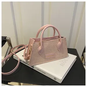 Detail of pink woven handbag with leather straps and metal fashion plaque on book