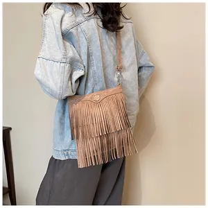 Close-up of brown suede crossbody bag featuring long bohemian tassels and gold metal logo