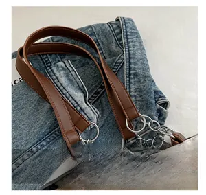 Detail of brown leather strap with silver metal rings and chain on beige tote bag