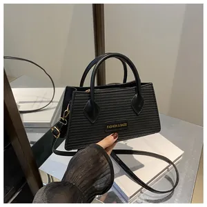 Detail of black textured crossbody bag with gold hardware and top handles on a mirror surface
