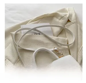 Close-up of white lychee leather texture and large gold square buckle on small handbag