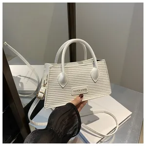 Close-up of white woven trapezoid handbag featuring gold hardware and a fashion label