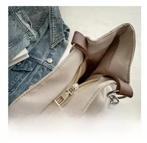 Detailed close-up of smooth metal zipper and brown leather trim on beige canvas tote bag