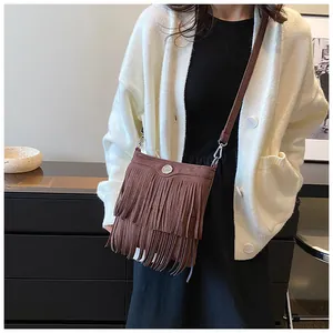 Detailed view of brown fringe crossbody bag with suede texture and metallic button