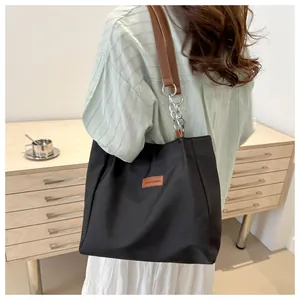 Detail of black nylon tote bag with brown leather logo patch and metal chain strap