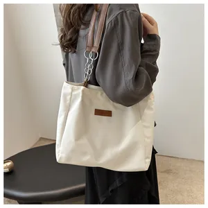 Detail of a cream tote bag featuring a brown leather and silver chain shoulder strap