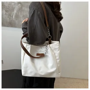 Detailed view of white tote bag with brown leather straps and silver metal chain accessory