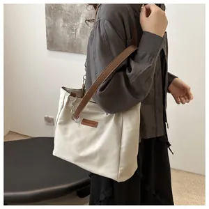 Detail of a cream tote bag with dark brown straps and metal chain accents shown on a model