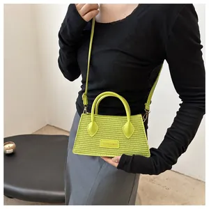 Detail of lime green woven tote bag with adjustable shoulder strap and leather logo tag