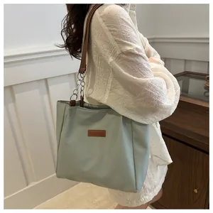 Detail of light green nylon tote bag with brown leather strap and silver chain link