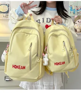 Detail view of large and small yellow nylon backpacks with HOKEAM logo and teddy charm