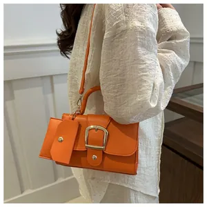 Detail view of orange crossbody bag with litchi texture and gold buckle on female model